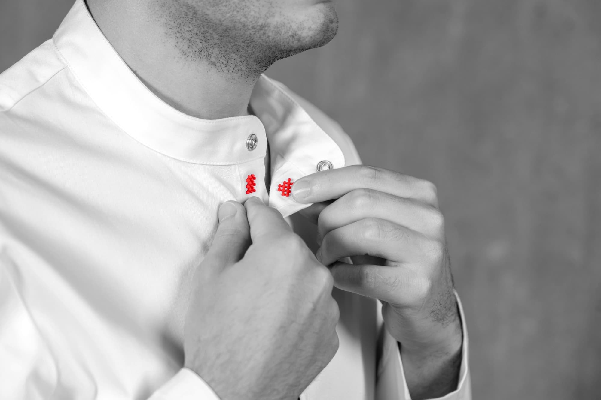 A chef buttoning a Gastrochef jacket with red detailing at the buttonholes