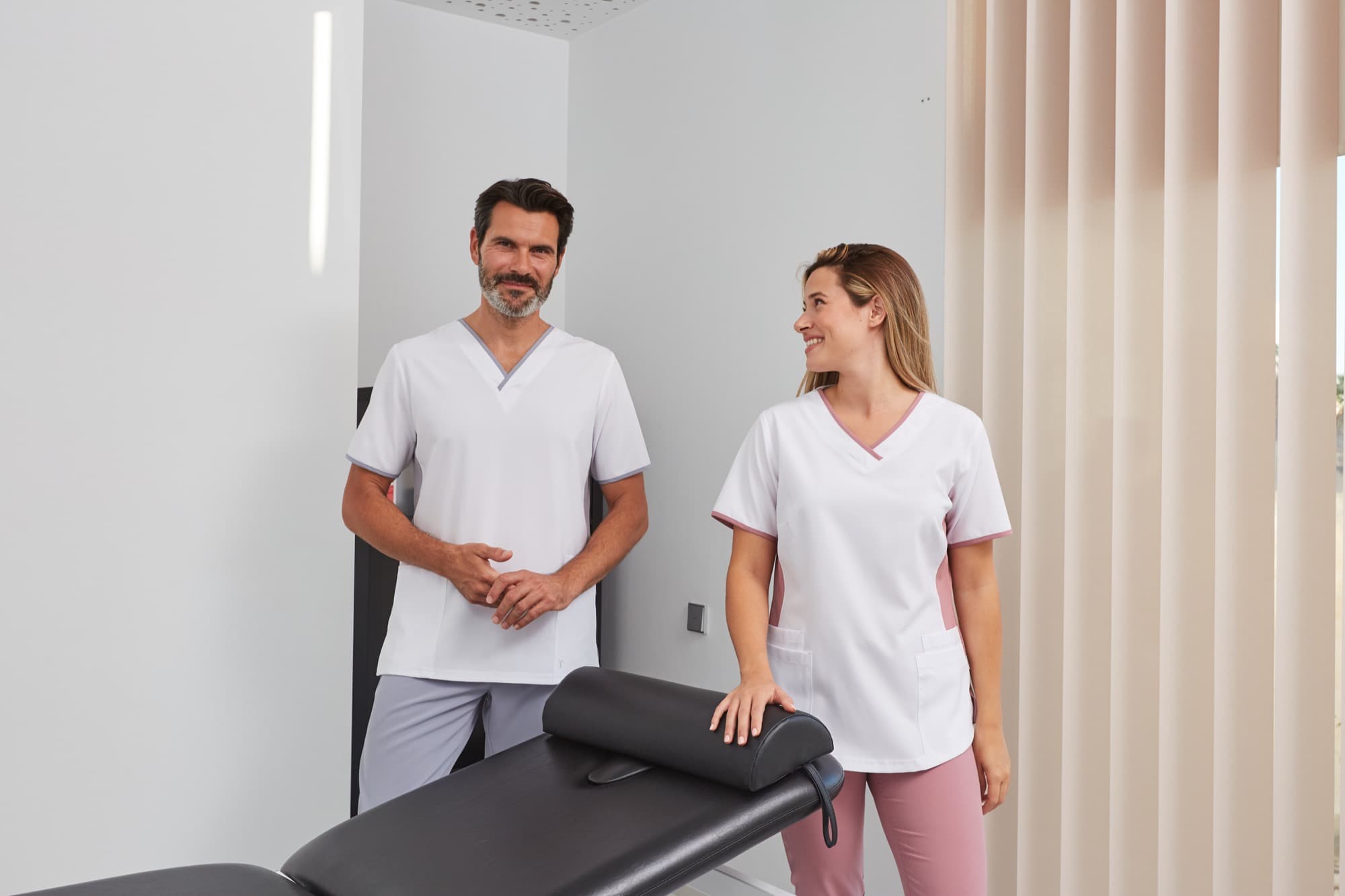 Δύο επαγγελματίες υγείας με μπλούζες Health & Wellness σε αίθουσα θεραπείας